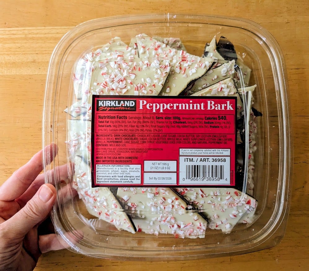 A hand holding a box of Costco Kirkland Peppermint Bark.