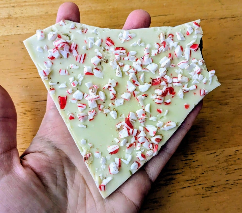A hand holding a large piece of Peppermint Bark from Costco.