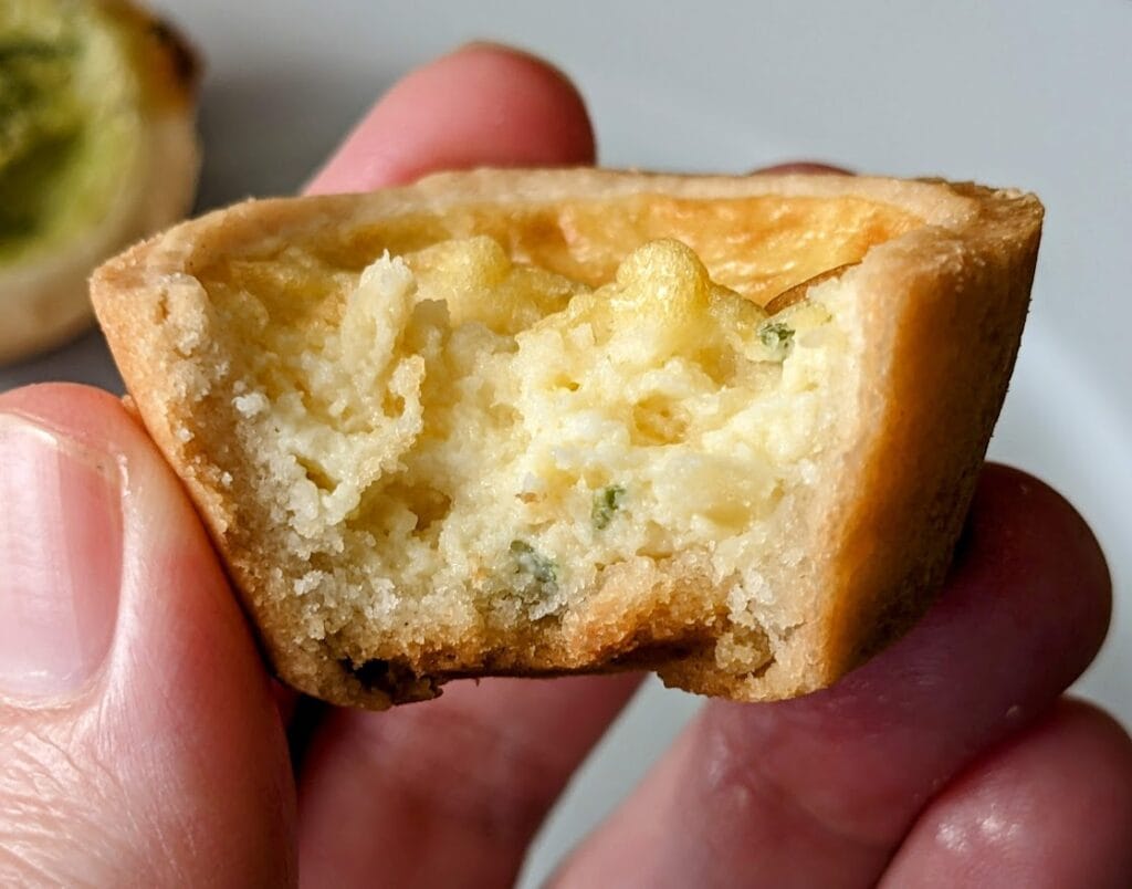 Fingers holding a bitten mini quiche from Cuisine Adventures.