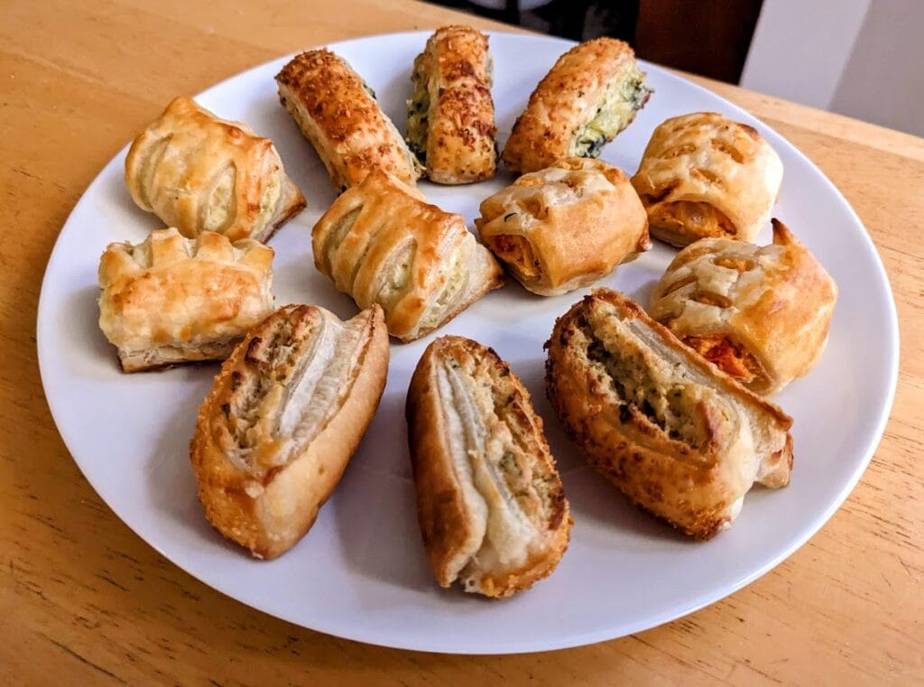 A white plate with 4 different kinds of Puff Pastry Bites from Cuisine Adventures.
