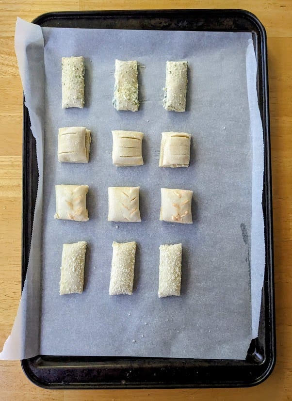A baking sheet lined with parchment with 12 frozen, raw puff pastry bites from Cuisine Adventures.