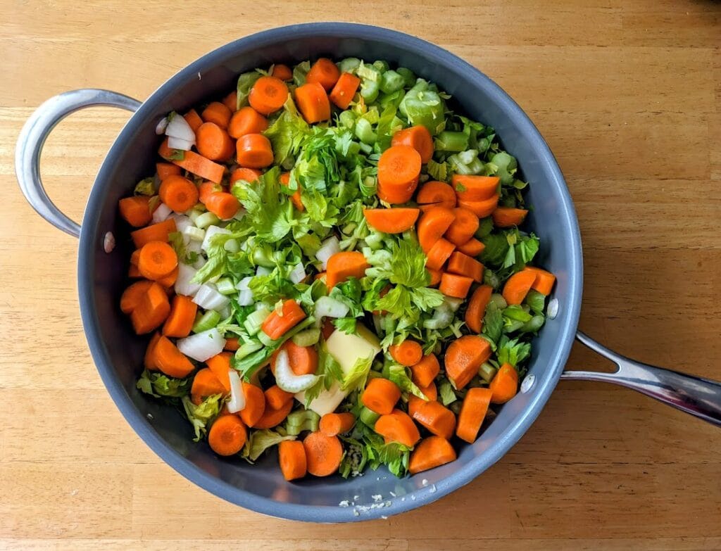 A large skillet with chopped carrots, celery, onions, and garlic.