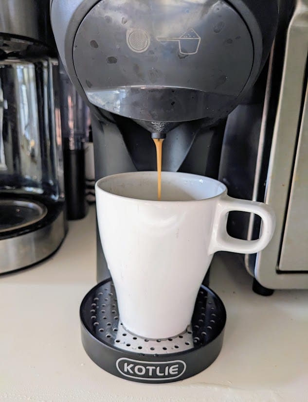 A white mug with a Kotlie nepresso capsule machine brewing coffee into the cup.