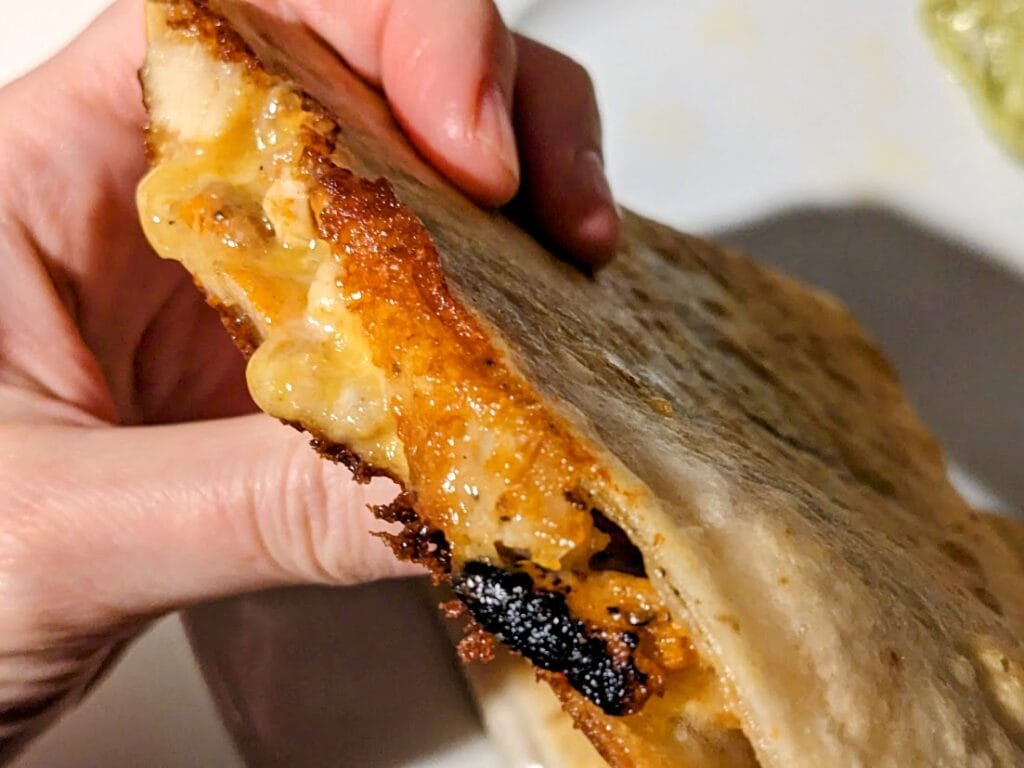 Fingers holding a cooked Chicken Quesadilla from Costco, showing melted cheese.