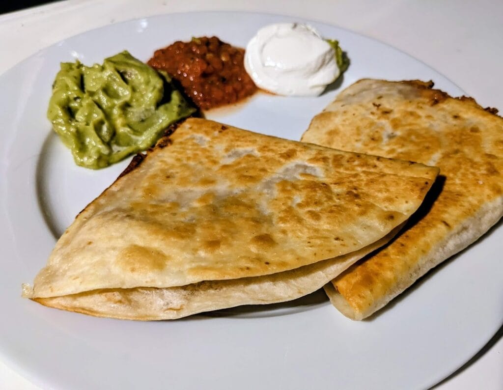 Two Costco Deli Chicken Quesadillas on a plate with guacamole, salsa, and sour cream.