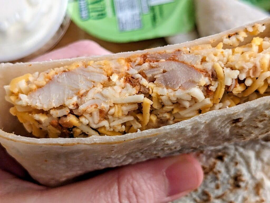 Fingers holding an uncooked Chicken Quesadilla from the Costco Deli, showing the cheese filling inside.