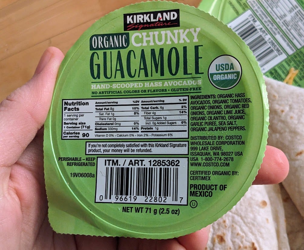 A hand holding a package of Costco Organic Chunky Guacamole.