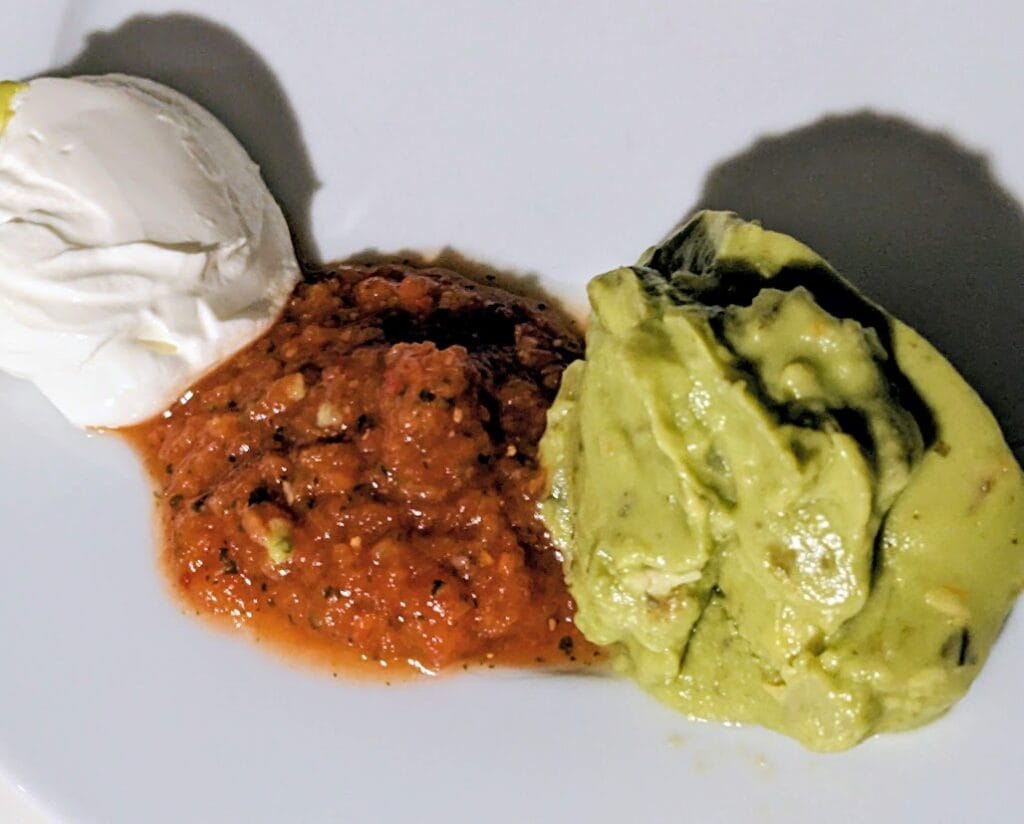 Sour cream, salsa, and guacamole on a white plate.