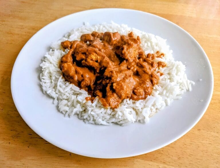 A white plate with basmati rice and Butter Chicken in sauce by Quicklly Indian Food (from Costco).