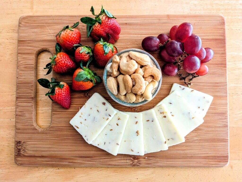 Overhead view of a charcuterie board with sliced Meister Caraway Cheddar cheese, cashews, strawberries, and grapes.