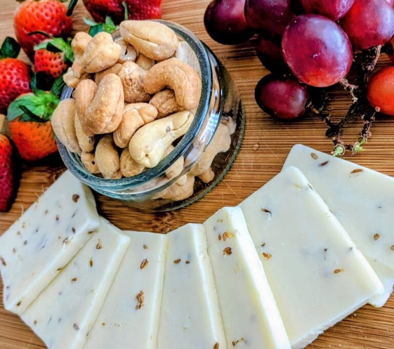 Close up of a charcuterie board with slices of Meister Caraway Cheddar Cheese, cashew nuts, grapes, and strawberries.