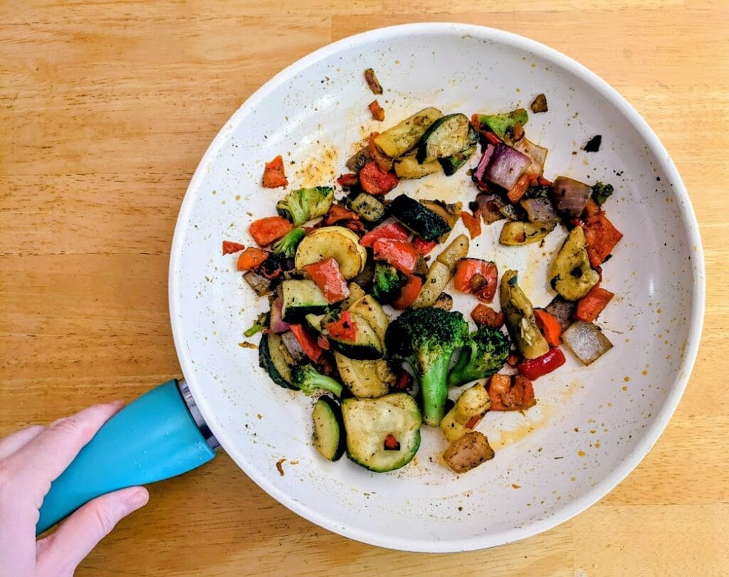 A hand holding a skillet with cooked fire roasted vegetable medley from Pura Vida.