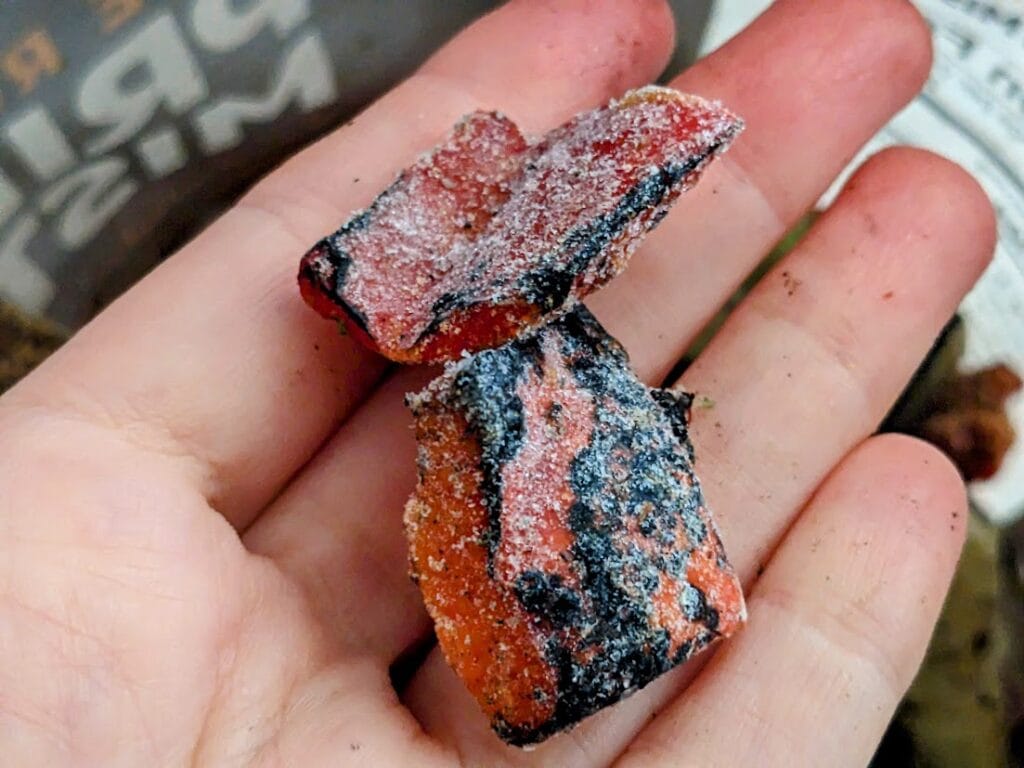 A hand holding two pieces of frozen fire roasted red bell pepper from a bag of Pura Vida Primavera Mistura.