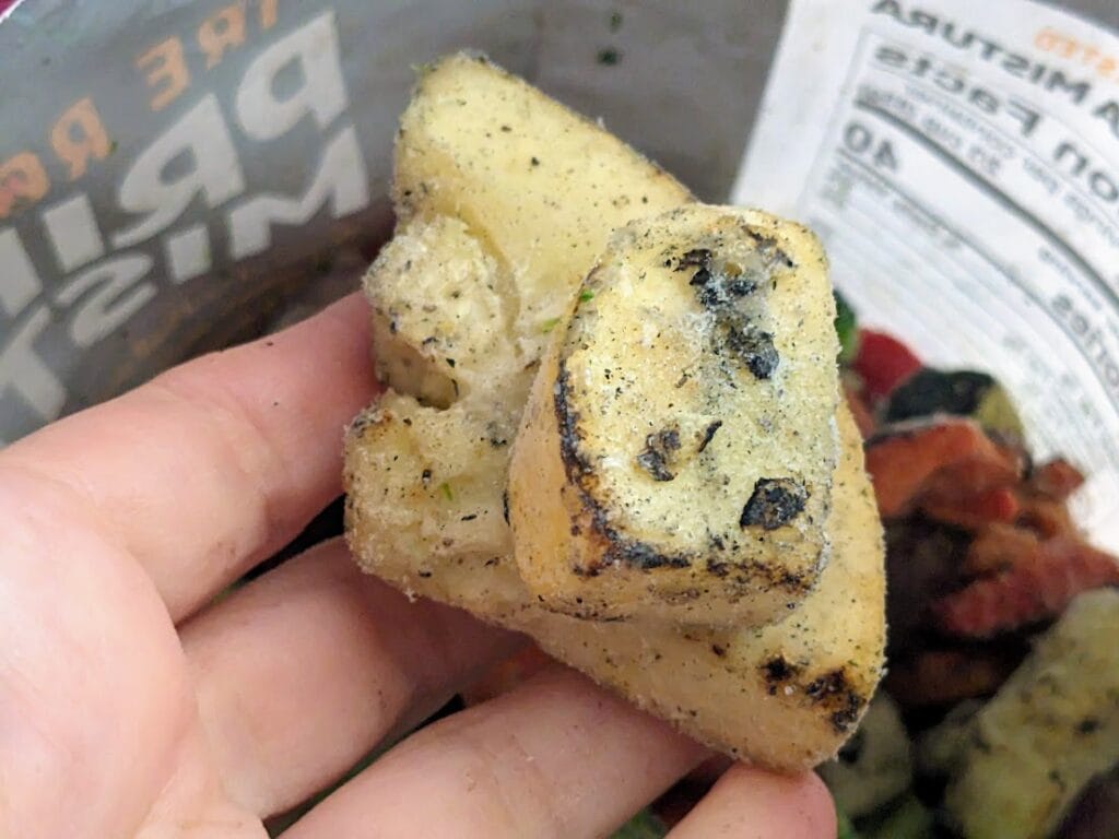 A hand holding a fire roasted yellow squash slice from a bag of frozen Pura Vida Primavera Mistura vegetables.