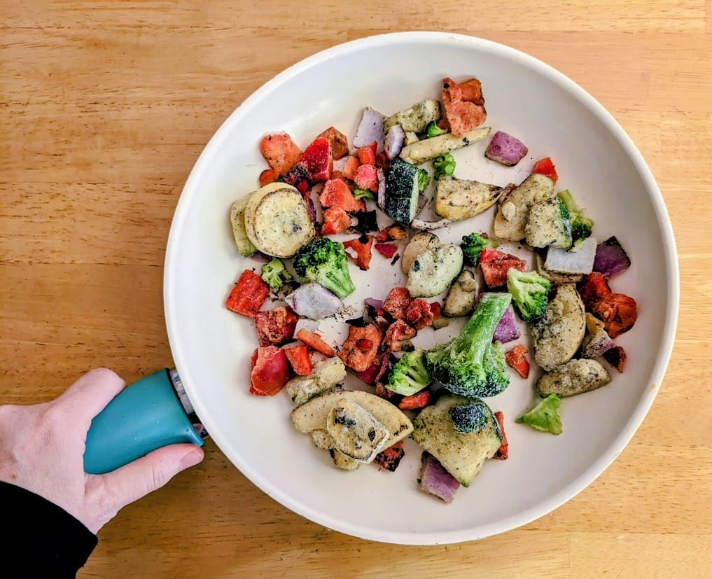 A hand holding a skillet with frozen Pura Vida Primavera Mistura fire roasted vegetables.