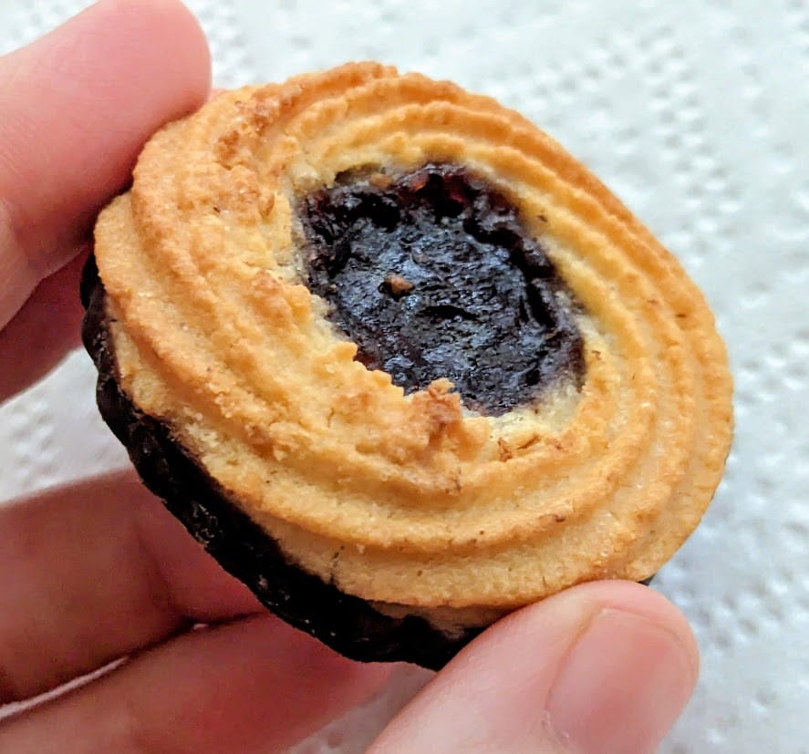 Fingers holding a Marzipan Cookie from Aldi with a berry jelly center.