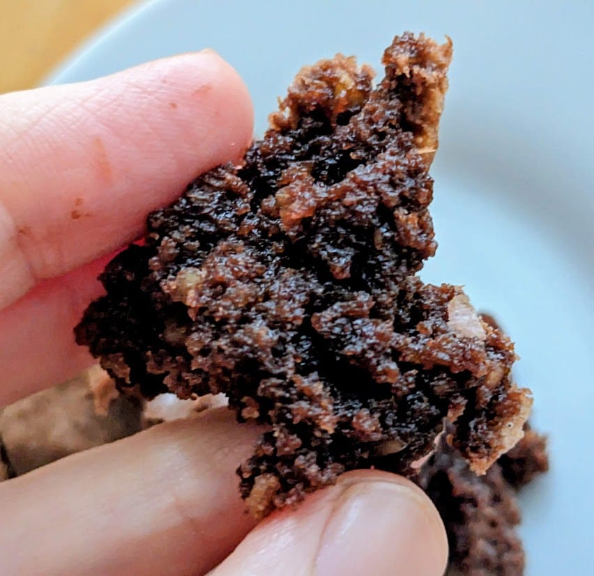 Fingers holding a piece of chewy fudge brownie baked from an Aldi mix.