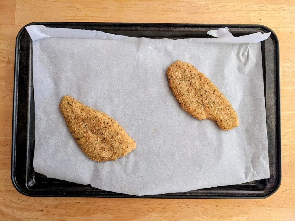 A parchment lined baking pan with two frozen Parmesan Crusted Flounder Fillets from Aldi.