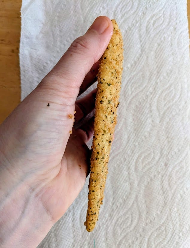 A hand holding a side view of a frozen, parmesan breaded flounder fillet from Aldi.