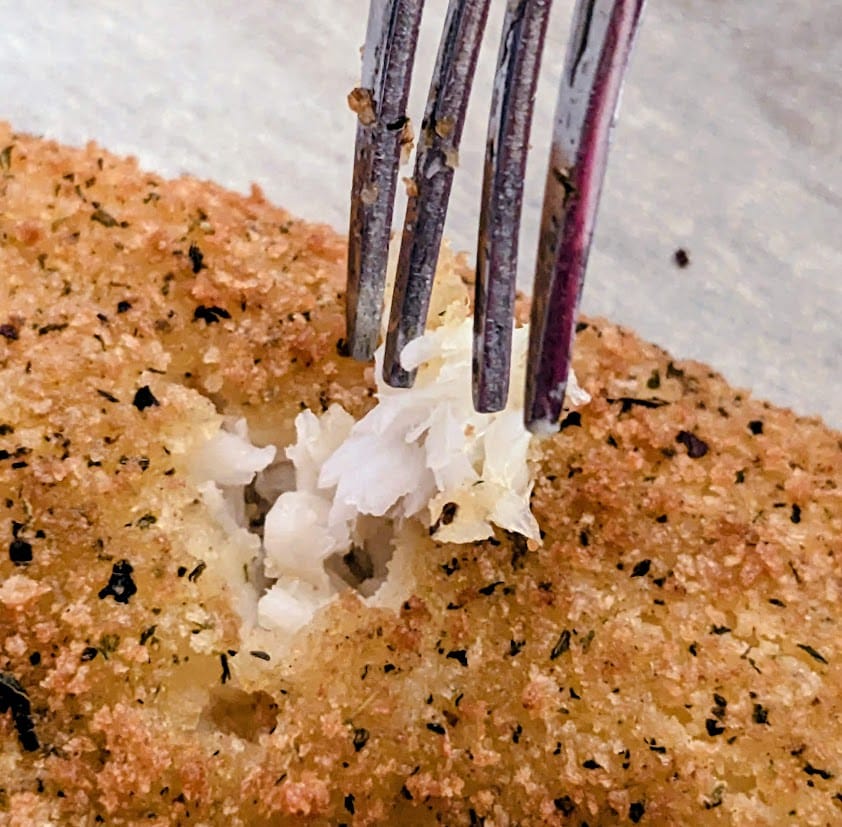 A fork flaking a baked fillet of parmesan breaded flounder from Aldi.