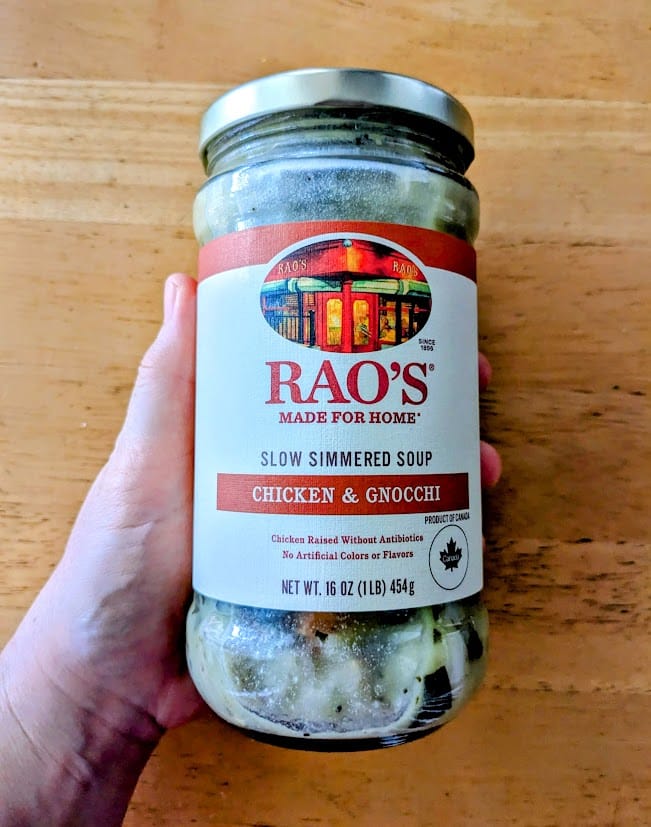A hand holding a jar of Rao's Chicken & Gnocchi Soup.