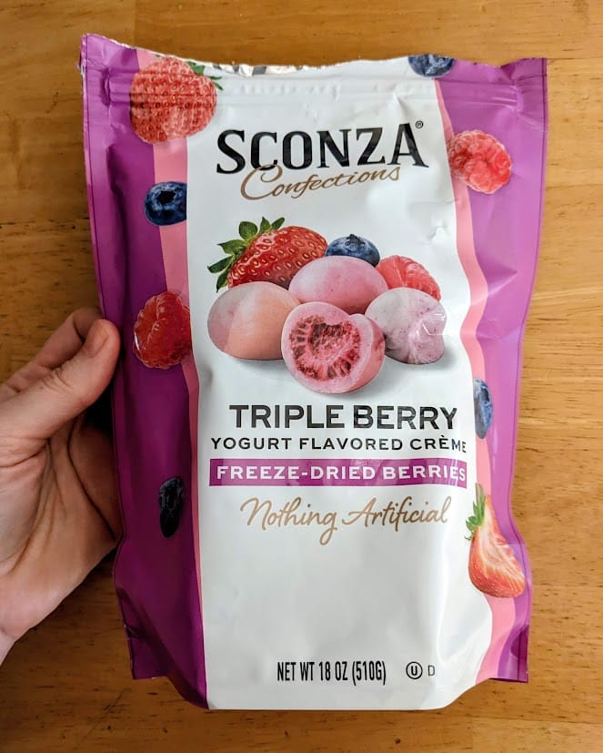 A hand holding a bag of Sconza Triple Berry Yogurt Creme Freeze-Dried Berries from Costco.