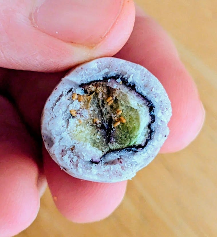 Fingers holding a bitten Sconza Yogurt Covered Freeze Dried Blueberry candy.