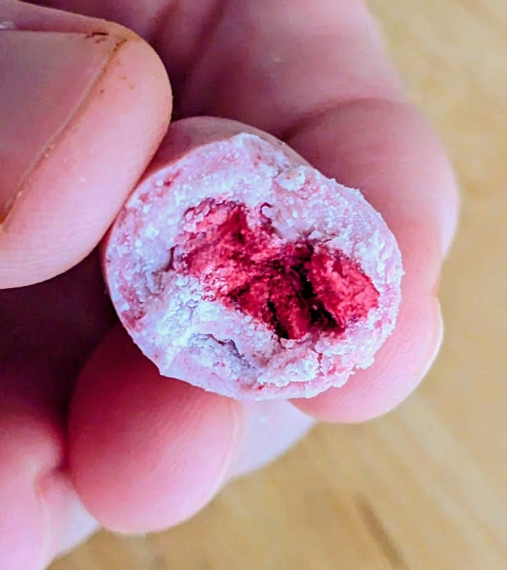 Fingers holding a pink bitten Sconza Yogurt Covered Raspberry.