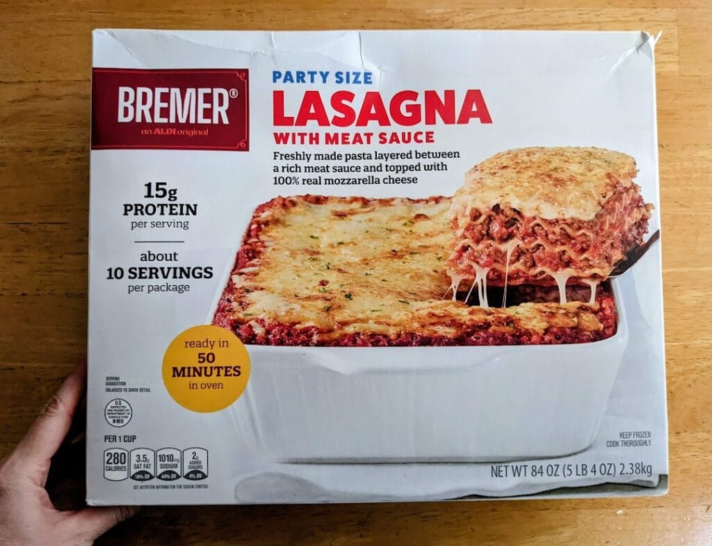 A hand holding a box of Aldi Bremer Party Size Lasagna with Meat Sauce.