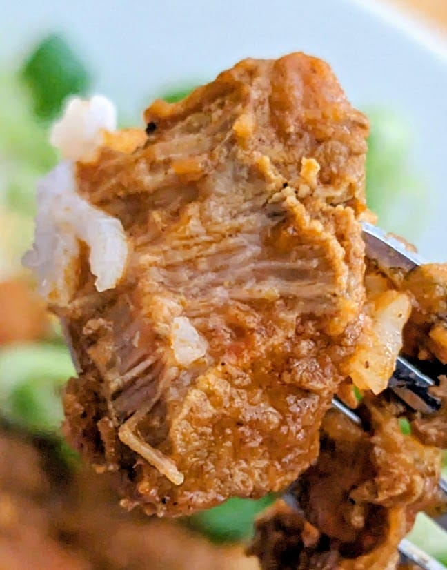 A fork holding a chunk of braised meat from a Quicklly Goanese Lamb Vindaloo curry meal.