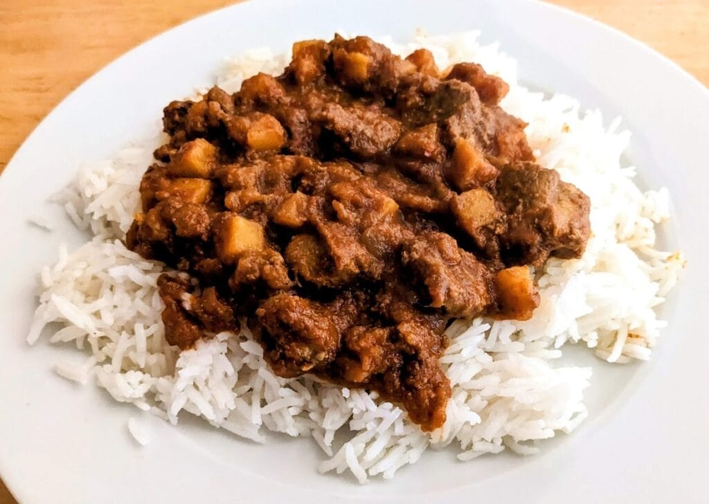 A white plate with basmati rice topped with Goanese Lamb Vindaloo curry from Quicklly Indian Food.