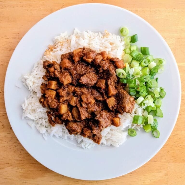 A white plate with rice, green onions, and Quicklly Indian Lamb Vindaloo Curry.
