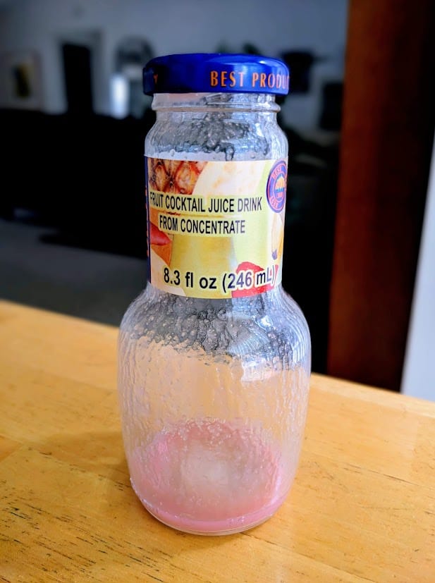 An empty bottle of BEST Egypt Canning Co Fruit Cocktail Juice Drink, sitting on a kitchen table.