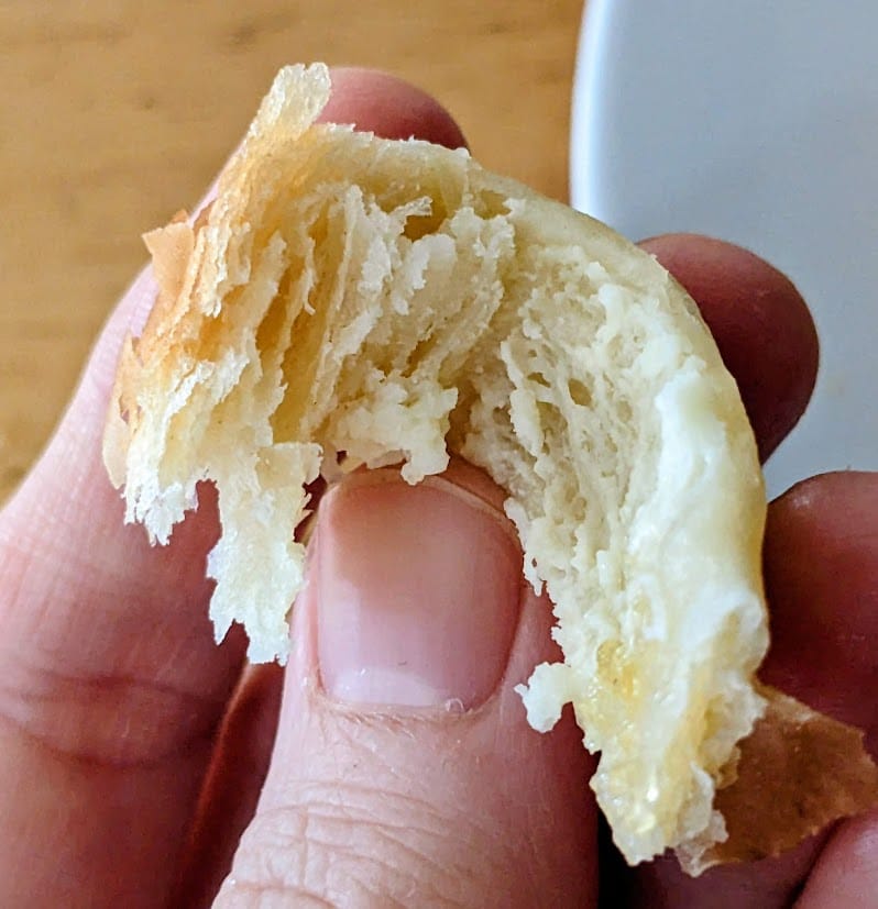 Fingers holding a flakey piece of a Costco Peaches and Cream pastry.