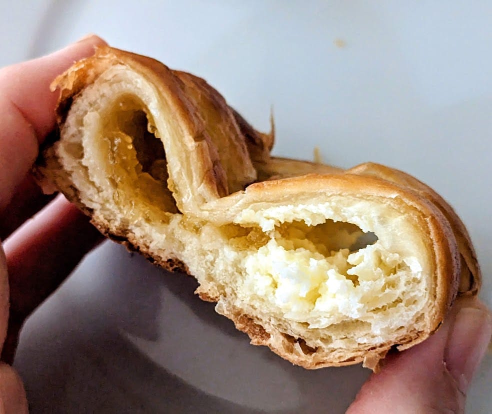 Fingers holding a cross section of a Costco Peaches and Cream Pastry, showing the filling.