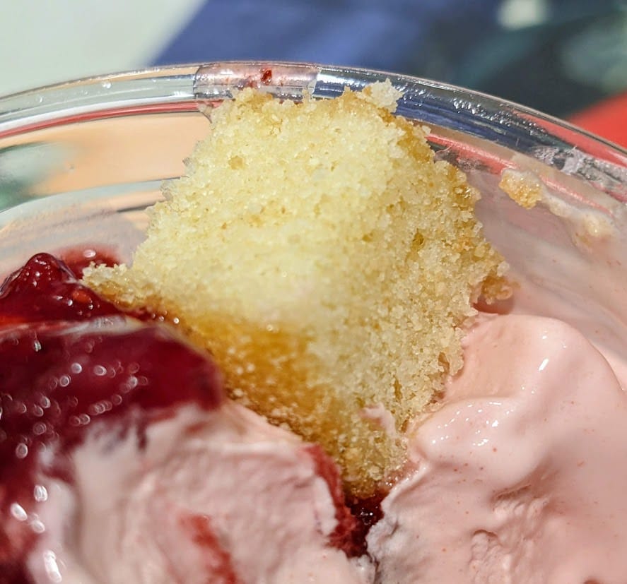 A cube of yellow cake on top of a pink Strawberry Shortcake Sundae from the Costco Foodcourt.
