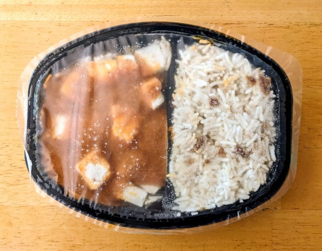 A frozen black plastic tray of Deep Indian Kitchen Paneer Tikka Masala, showing sauce and rice compartments.