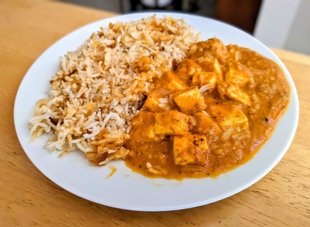 A white plate with a Paneer Tikka Masala meal from Deep Indian Kitchen.