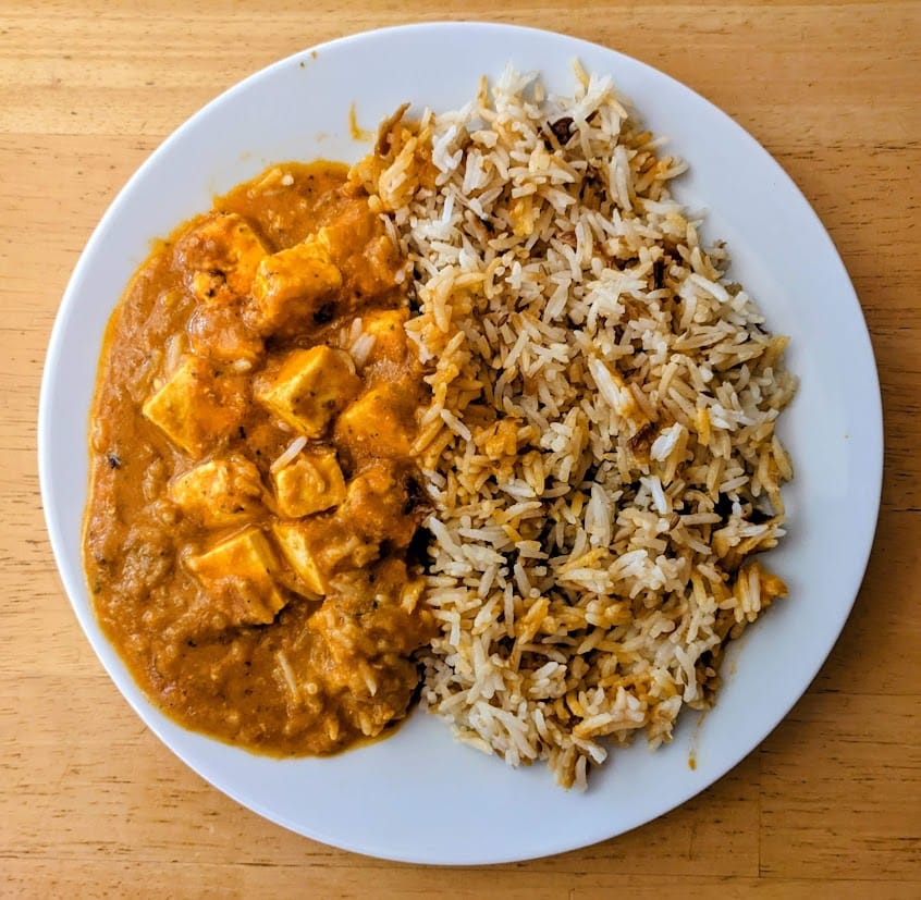 A white plate with a serving of Paneer Tikka Masala and Onion Basmati Rice from Deep Indian Kitchen.
