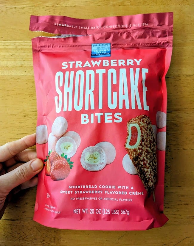 A hand holding a pink bag of Strawberry Shortcake Bites from Edward Marc Chocolatiers from Costco.
