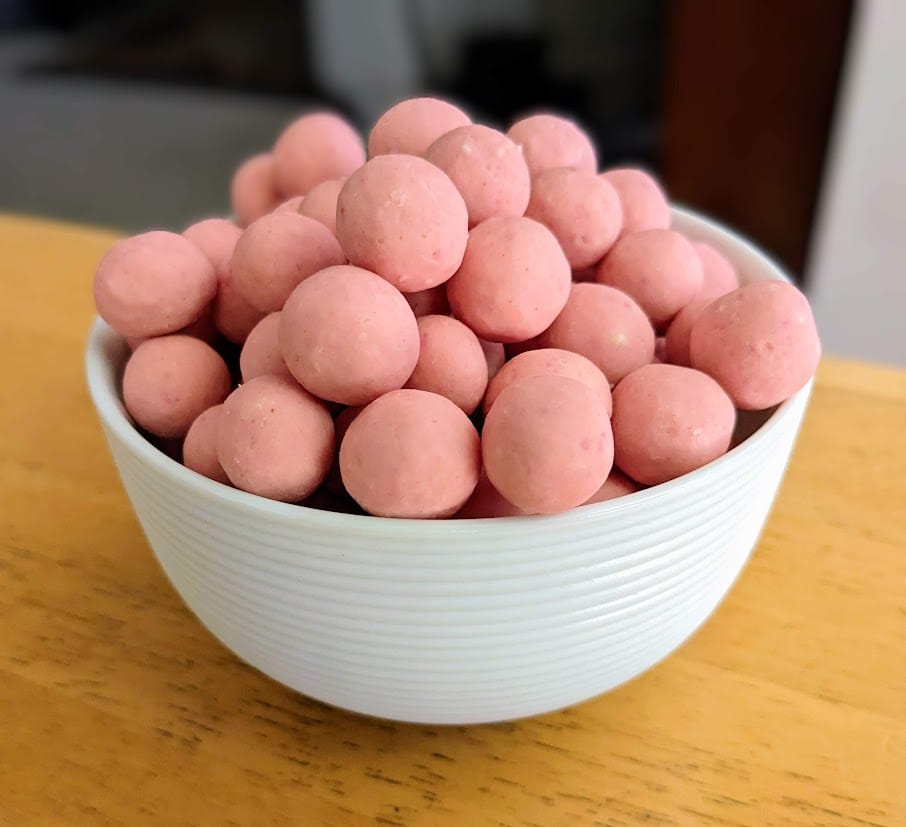 A white bowl filled with pink spherical Strawberry Shortcake Bites candies by Edward Marc Chocolatiers.