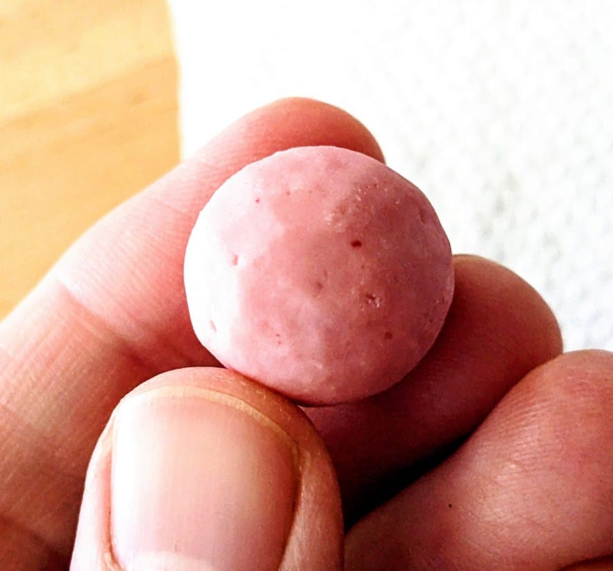 Fingers holding a small round pink Strawberry Shortcake Bite creme covered cookie.
