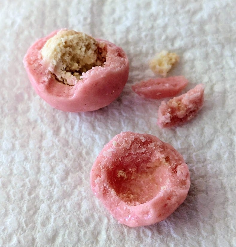 A deconstructed Strawberry Shortcake Bite from Edward Marc, showing the creme shell coating removed from the vanilla shortbread cookie center.