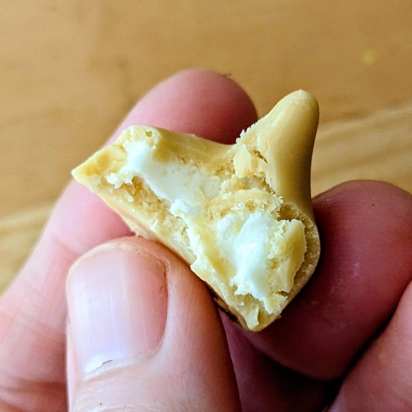 Fingers holding a bitten Hershey's Butterbeer Kiss, showing the white creme center.