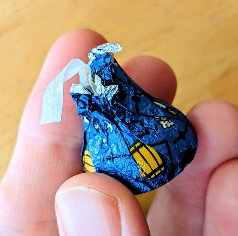 Fingers holding a blue foil wrapped Hershey's Butterbeer Kiss.