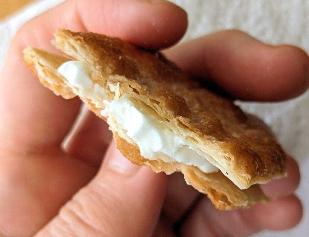 Fingers holding a bitten Karens Bakery Danish Puff Pastry Cookie, showing the lemon creme filling.