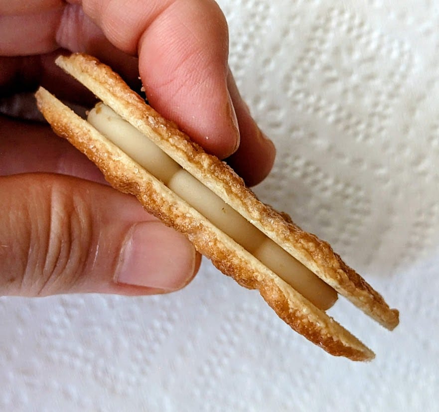 Fingers holding a side view of a Lemon flavor Danish Puff Pastry Cookie from Karens Bakery.