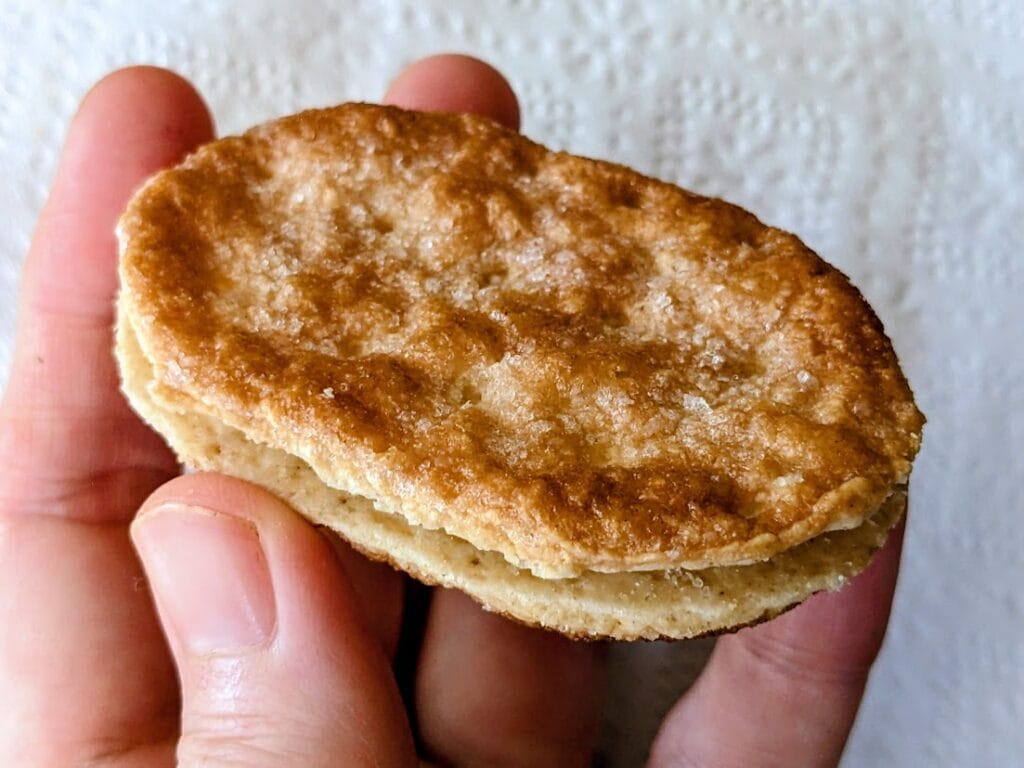 A hand holding a whole Danish Puff Pastry cookie from Karens Bakery.