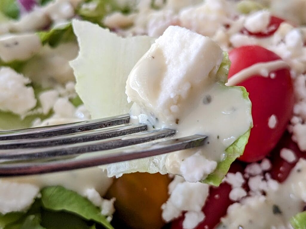 A fork holding a bite of salad with a chunk of President Crumbled Feta cheese.