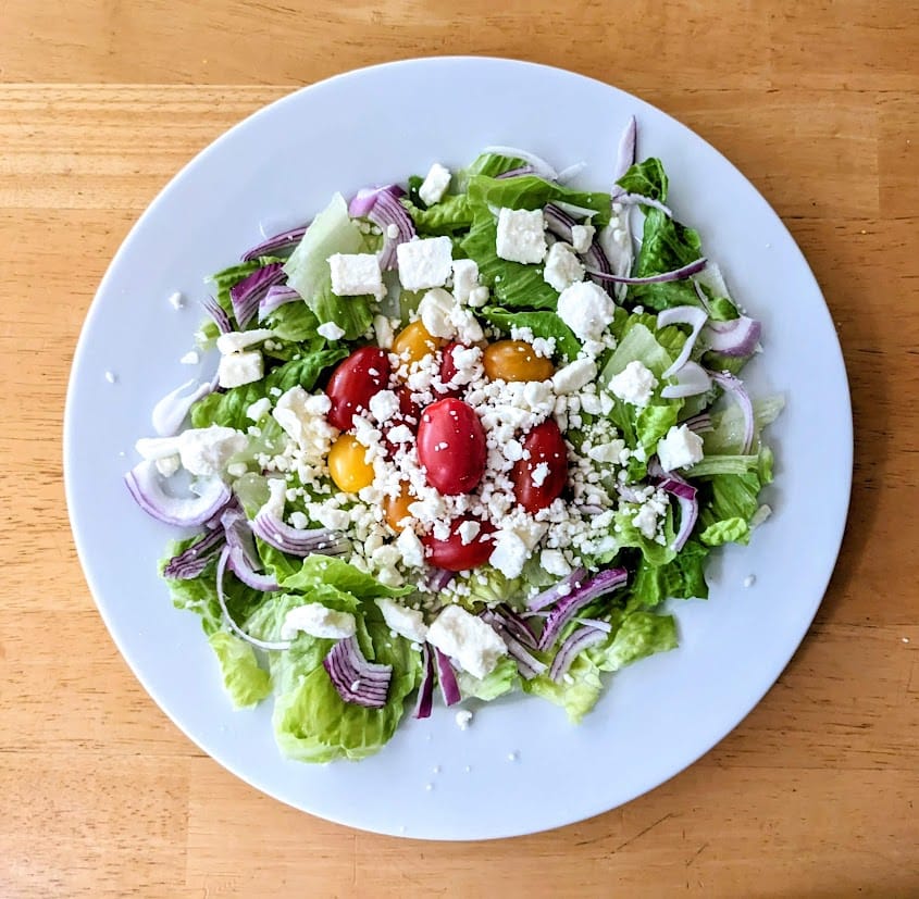 A white plate with a salad topped with President Feta Crumbles.